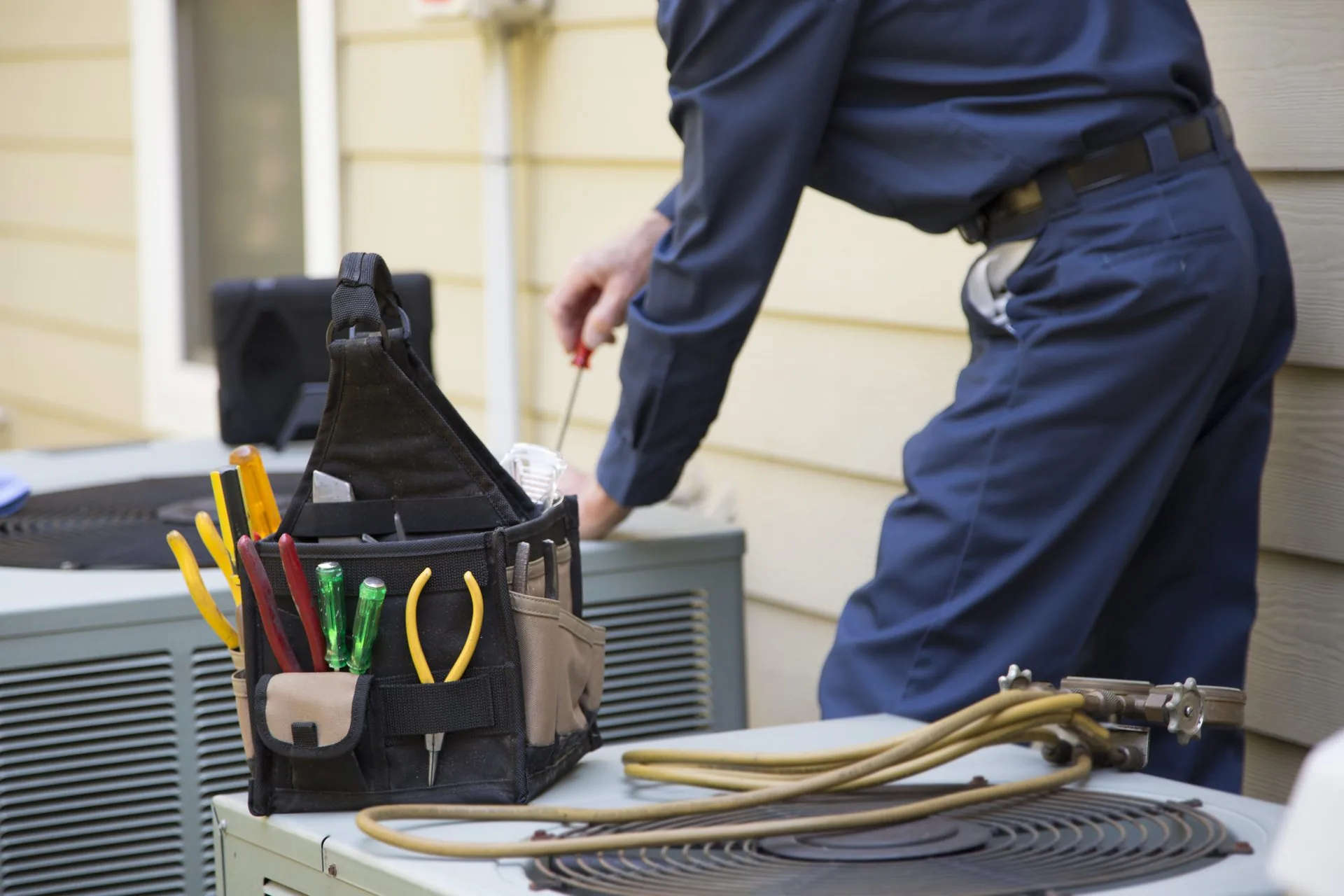 HVAC technician servicing an outdoor air conditioning unit with professional tools